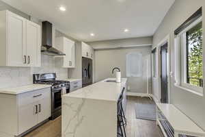 Kitchen with stainless steel appliances, wall chimney exhaust hood, a sink, white cabinetry, and recessed lighting