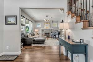 Living area featuring dark wood finished floors, plenty of natural light, stairway, and an inviting chandelier
