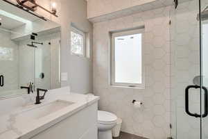 Bathroom featuring tile walls, a shower stall, toilet, and vanity