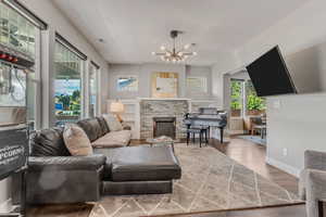 Living area with visible vents, baseboards, a notable chandelier, wood finished floors, and a stone fireplace