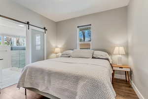 Bedroom featuring a barn door, light wood-type flooring, access to exterior, and baseboards