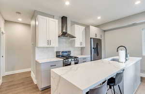 Kitchen with wall chimney exhaust hood, appliances with stainless steel finishes, baseboards, light wood-type flooring, and a sink
