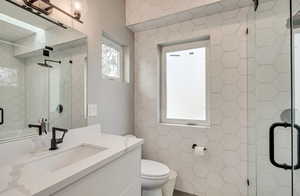 Full bath featuring a stall shower, tile walls, toilet, and vanity