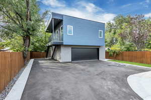 View of side of property featuring stairs, an attached garage, fence, and asphalt driveway