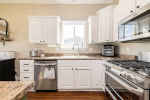 Kitchen with appliances with stainless steel finishes, a sink, white cabinetry, and dark wood-style floors