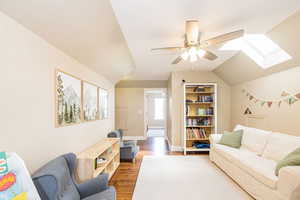 Living room featuring a skylight, ceiling fan, wood finished floors, baseboards, and lofted ceiling