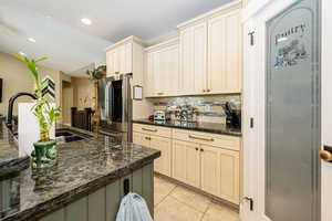 Kitchen with stainless steel fridge, cream cabinets, decorative backsplash, a sink, and light tile patterned floors