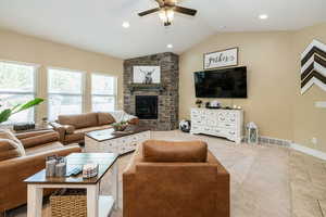 Living room featuring ceiling fan, healthy amount of natural light, lofted ceiling, a stone fireplace, and recessed lighting
