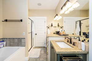Primary Bathroom featuring stone tile flooring, a shower stall, a garden tub, vanity, and a chandelier