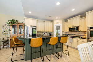 Kitchen with stainless steel appliances, cream cabinetry, tasteful backsplash, light tile patterned floors, and a kitchen island with sink