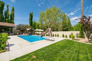 View of pool with a gazebo, a water slide, and a patio, with small grass area.