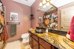 ADU Bathroom with toilet, vanity, stone finish flooring, a chandelier, and baseboards