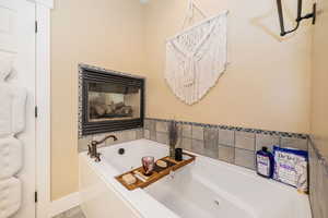 Primary Full bath featuring a tub with jets, baseboards, and a multi sided fireplace