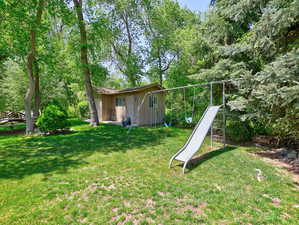 View of green lawn featuring a playground and an outdoor structure
