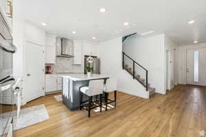 Kitchen with wall chimney exhaust hood, stainless steel appliances, a center island, white cabinets, and recessed lighting