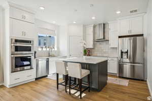 Kitchen featuring appliances with stainless steel finishes, wall chimney exhaust hood, a sink, tasteful backsplash, and white cabinets