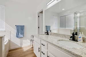 Bathroom with wood finished floors, double vanity, a shower stall, and baseboards