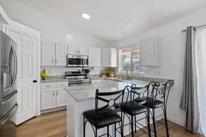 Kitchen featuring stainless steel appliances, a sink, a kitchen breakfast bar, vaulted ceiling, and white cabinets