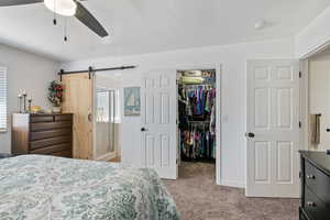 Bedroom featuring a barn door, light carpet, a spacious closet, a closet, and a ceiling fan