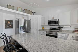 Kitchen featuring stainless steel appliances, white cabinets, vaulted ceiling, and light stone counters