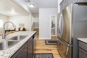 Kitchen featuring stainless steel appliances, a sink, light wood-style floors, baseboards, and light stone countertops