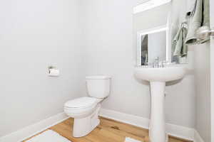 Half bathroom featuring wood finished floors, baseboards, and toilet