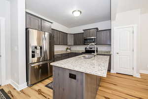 Kitchen with appliances with stainless steel finishes, light wood-style floors, dark brown cabinetry, and baseboards