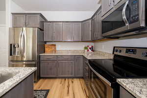 Kitchen featuring stainless steel appliances, light wood-type flooring, dark brown cabinetry, and light stone countertops