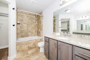 Full bath featuring a spacious closet, tiled shower / bath, vanity, toilet, and baseboards