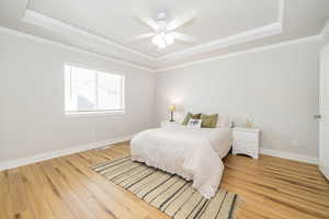 Bedroom featuring a tray ceiling, light wood-style flooring, crown molding, baseboards, and ceiling fan