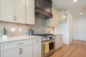 Kitchen featuring high end stainless steel range oven, custom range hood, light wood finished floors, decorative backsplash, and recessed lighting
