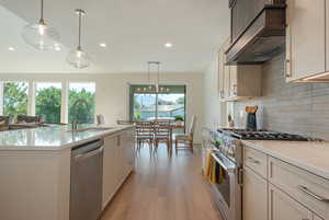 Kitchen with pendant lighting, stainless steel appliances, tasteful backsplash, wall chimney exhaust hood, and light stone counters