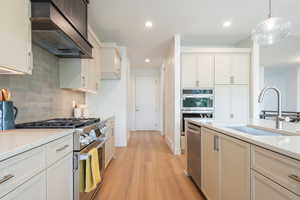 Kitchen featuring appliances with stainless steel finishes, wall chimney range hood, light wood-style flooring, pendant lighting, and recessed lighting