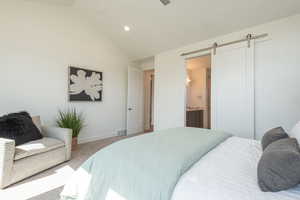 Carpeted bedroom with a barn door, lofted ceiling, recessed lighting, ensuite bath, and ceiling fan