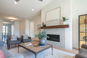 Living area featuring light wood-style flooring, a tile fireplace, lofted ceiling, recessed lighting, and a ceiling fan