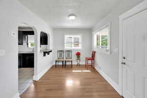 Living area featuring light wood-style flooring, a textured ceiling, arched walkways, and baseboards