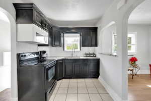 Kitchen with black range with electric cooktop, white microwave, a sink, arched walkways, and plenty of natural light