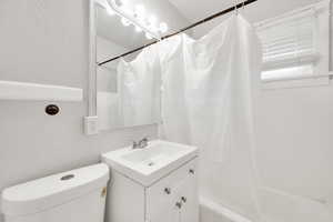 Full bath featuring toilet, vanity, a textured wall, and shower / bathtub combination with curtain