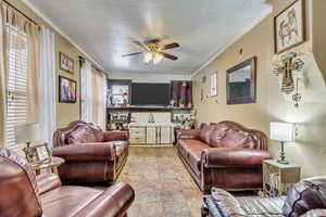 Living room with ornamental molding, a ceiling fan, and light stone finish flooring