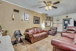 Living room featuring ceiling fan, stone finish floors, ornamental molding, and baseboards