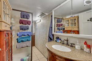 Bathroom featuring tile walls, tile patterned flooring, vanity, and decorative backsplash
