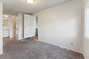 Carpeted spare room featuring a textured ceiling and baseboards