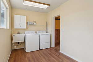 Clothes washing area featuring washing machine and dryer, wood finished floors, cabinet space, and baseboards