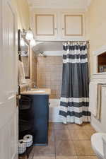 Bathroom featuring tile patterned floors, shower / bath combination with curtain, vanity, crown molding, and toilet