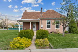 View of front of home with a front lawn, brick siding, a porch, a mountain view, and roof with shingles