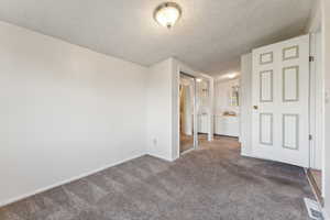 Unfurnished bedroom featuring carpet floors, a textured ceiling, baseboards, and connected bathroom