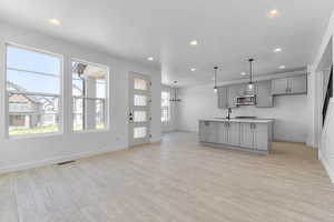 Kitchen with gray cabinets, stainless steel microwave, recessed lighting, baseboards, and light wood finished floors