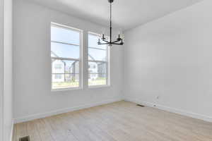 Spare room featuring a chandelier, light wood-type flooring, baseboards, and a textured ceiling