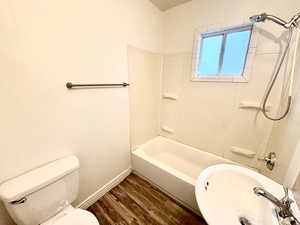 Full bath with wood finished floors, a sink, toilet, baseboards, and washtub / shower combination