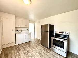Kitchen featuring appliances with stainless steel finishes, washing machine and dryer, light wood-style floors, light countertops, and white cabinetry